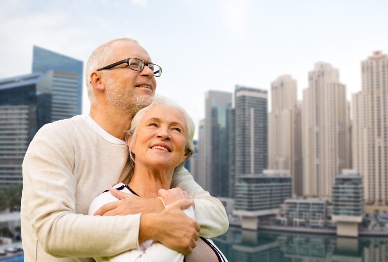 family, age, tourism, travel and people concept - senior couple hugging over dubai city waterfront background